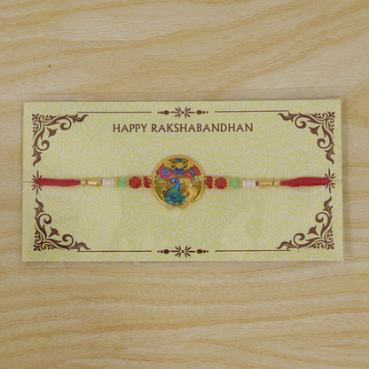 A red thread bracelet with a colorful peacock and floral design is presented on a yellow