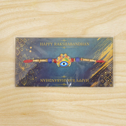 The Evil Eye Rakhi, with its blue eye and colorful leaf design, is displayed on a dark blue card with
