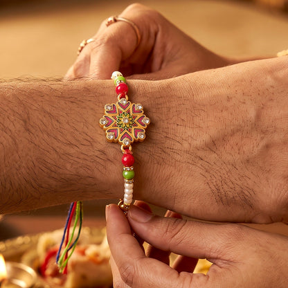 A person's hand tying a floral Kundan bracelet with colorful beads and pearls onto another person's wrist.