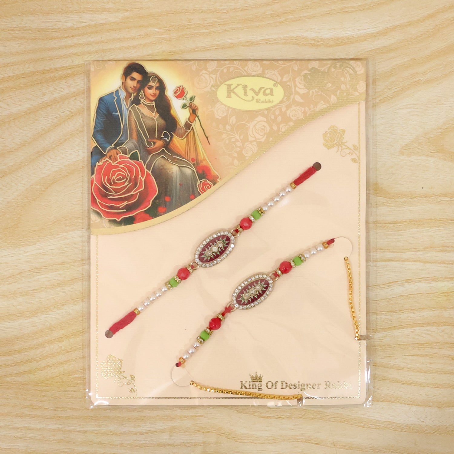 Two red and gold beaded bracelets with oval centers are packaged on a card with an illustration of a couple, on a wooden