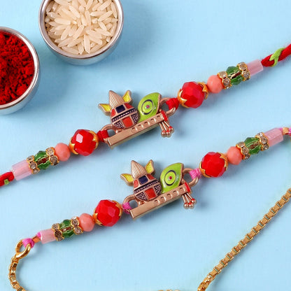 Two colorful Kalash motif bracelets with red, pink, and green beads lie on a blue surface, next to bowls of rice and red