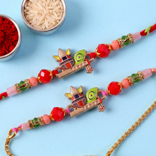 Two colorful Kalash motif bracelets with red, pink, and green beads lie on a blue surface, next to bowls of rice and red