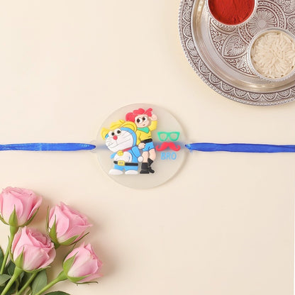 Doraemon and Nobita Rakhi with a 'BRO' charm, displayed on a light background with pink roses and a puja thali.
