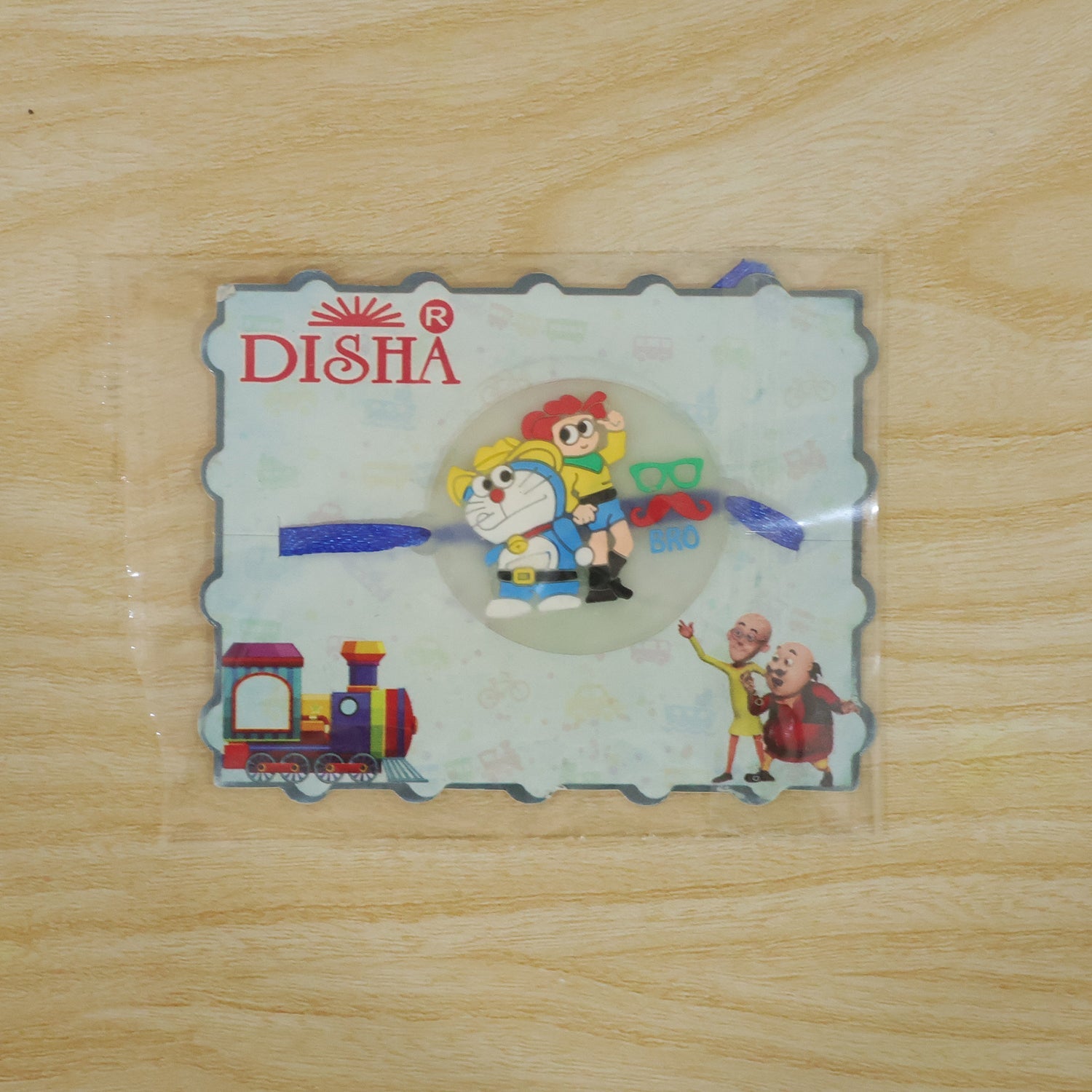 The Doraemon and Nobita Rakhi with a 'BRO' charm, packaged in a clear plastic sleeve with a DISHA branded card.