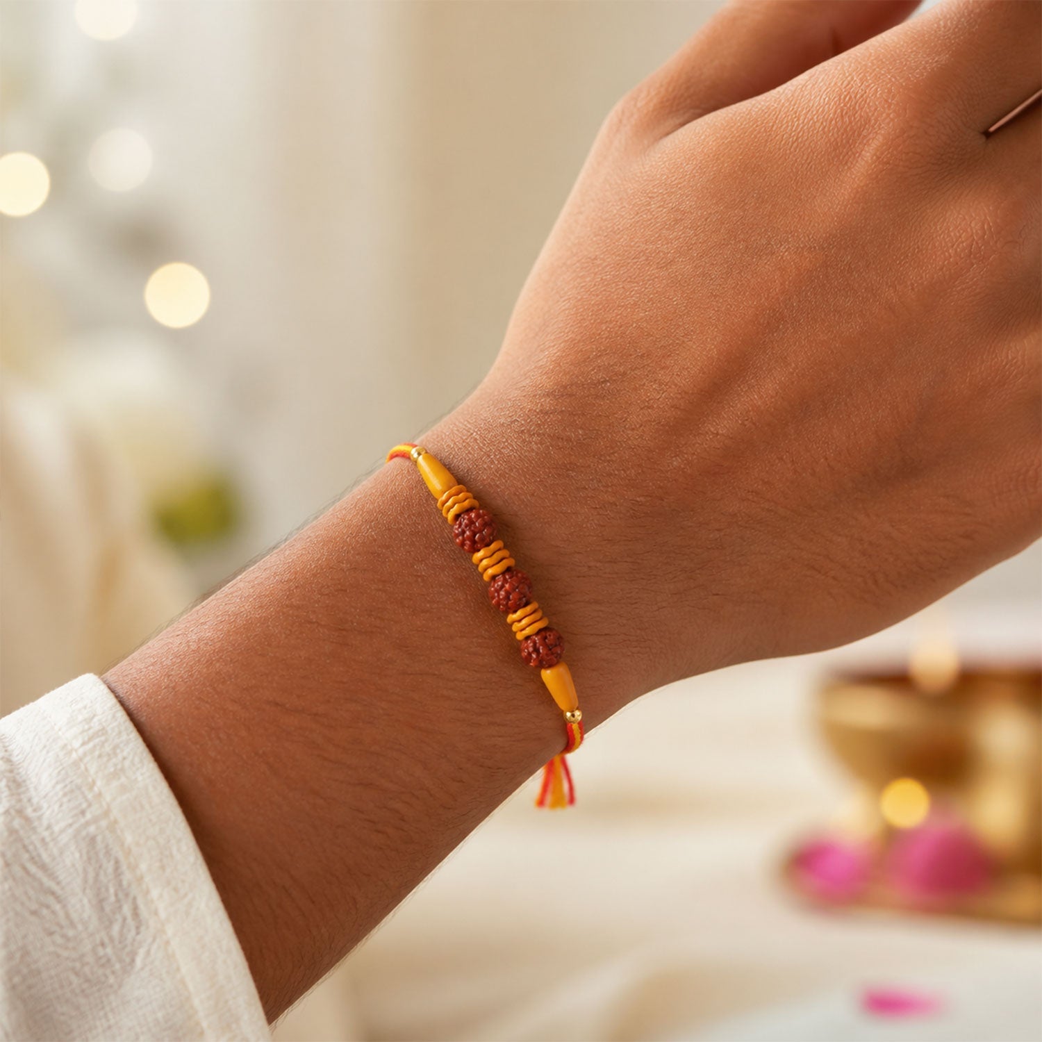 A Rudraksha Rakhi with three textured brown beads and wavy light brown spacers on a red and yellow thread, worn on a
