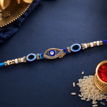 A blue evil eye rakhi with a gold and rhinestone center charm, accented with smaller blue evil eye beads and white and gold