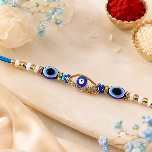 A blue evil eye rakhi with a gold and rhinestone center charm, surrounded by smaller blue evil eye beads and white and gold