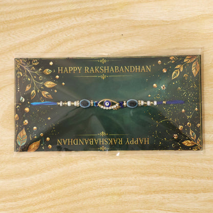 A blue evil eye rakhi with a gold and rhinestone center charm, along with smaller blue evil eye beads and white and gold