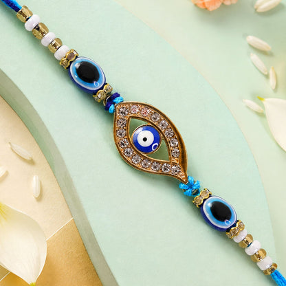 A blue evil eye rakhi with a stone-studded center charm on a light green background with white flower petals.