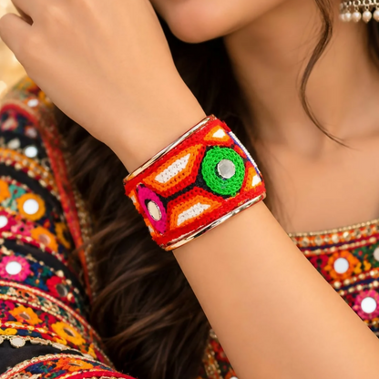 A woman's arm wearing a colorful embroidered cuff bracelet with mirror accents, complementing her patterned attire.