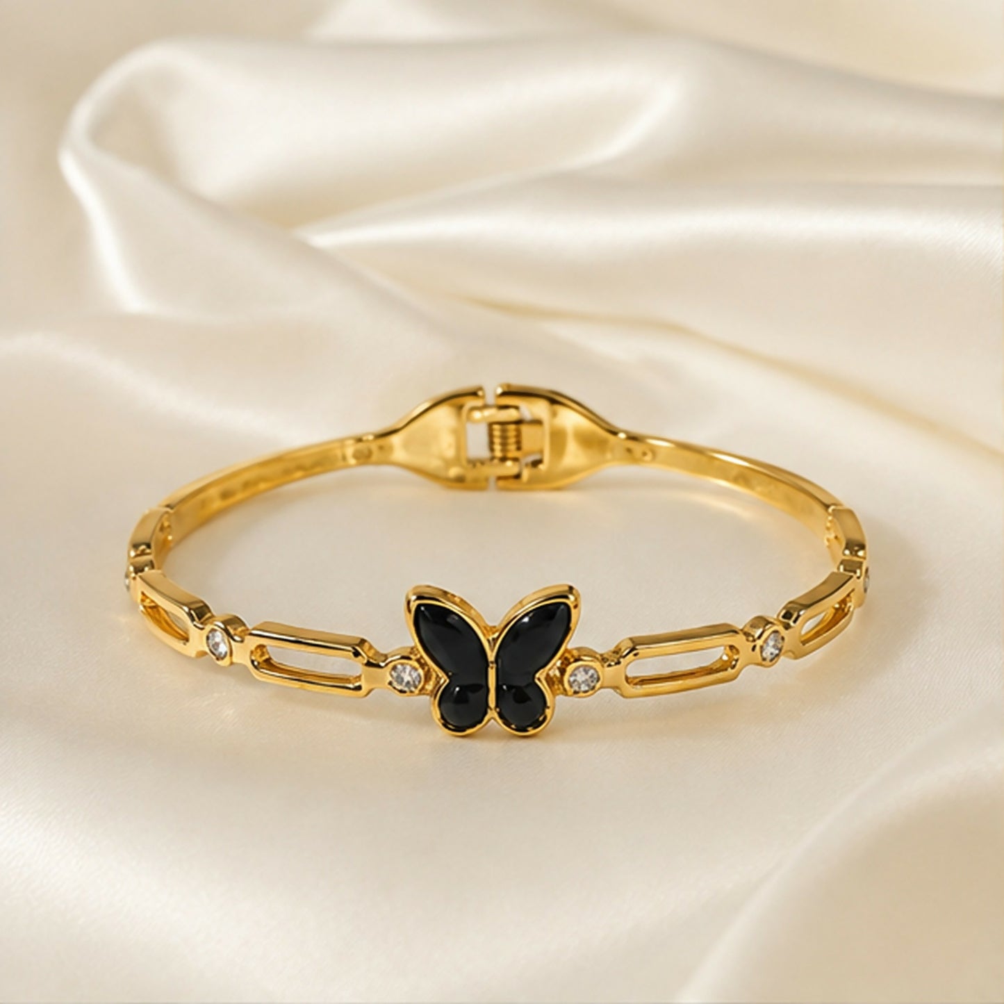 The gold-tone bracelet with a black butterfly charm and crystal accents is showcased on a white satin surface.
