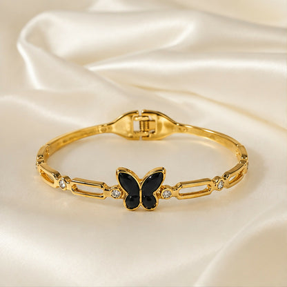 The gold-tone bracelet with a black butterfly charm and crystal accents is showcased on a white satin surface.