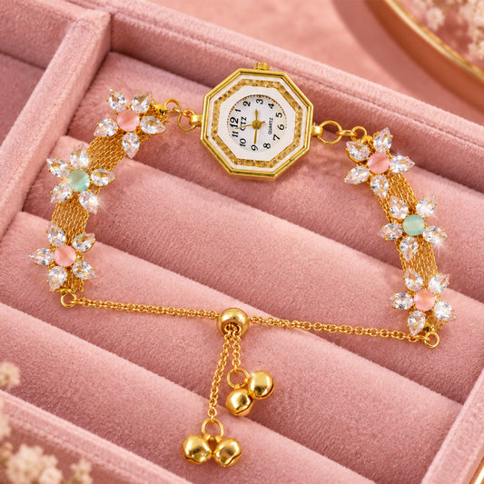 A gold-tone bracelet watch with an octagonal dial and crystal flower accents rests on a pink velvet jewelry box.