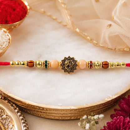 Om Sacred Symbol Golden Devotional Rakhi with Peach Beads and Red Thread