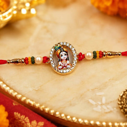 A red thread bracelet with a gold oval Bal Krishna charm, pearls, and colorful beads is on a gold-rimmed white marble tray