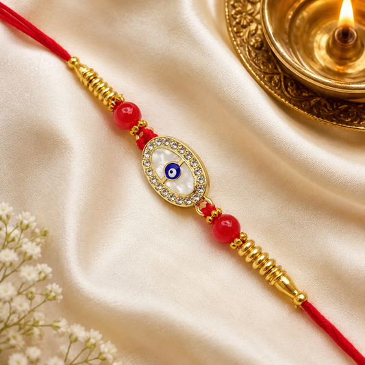 A red thread bracelet with a golden oval charm featuring a blue evil eye, white stones, and red beads rests on a cream silk