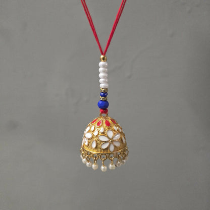A gold-finished lumba with white and red enamel flowers, pearl drops, and a red thread hangs against a plain gray background.
