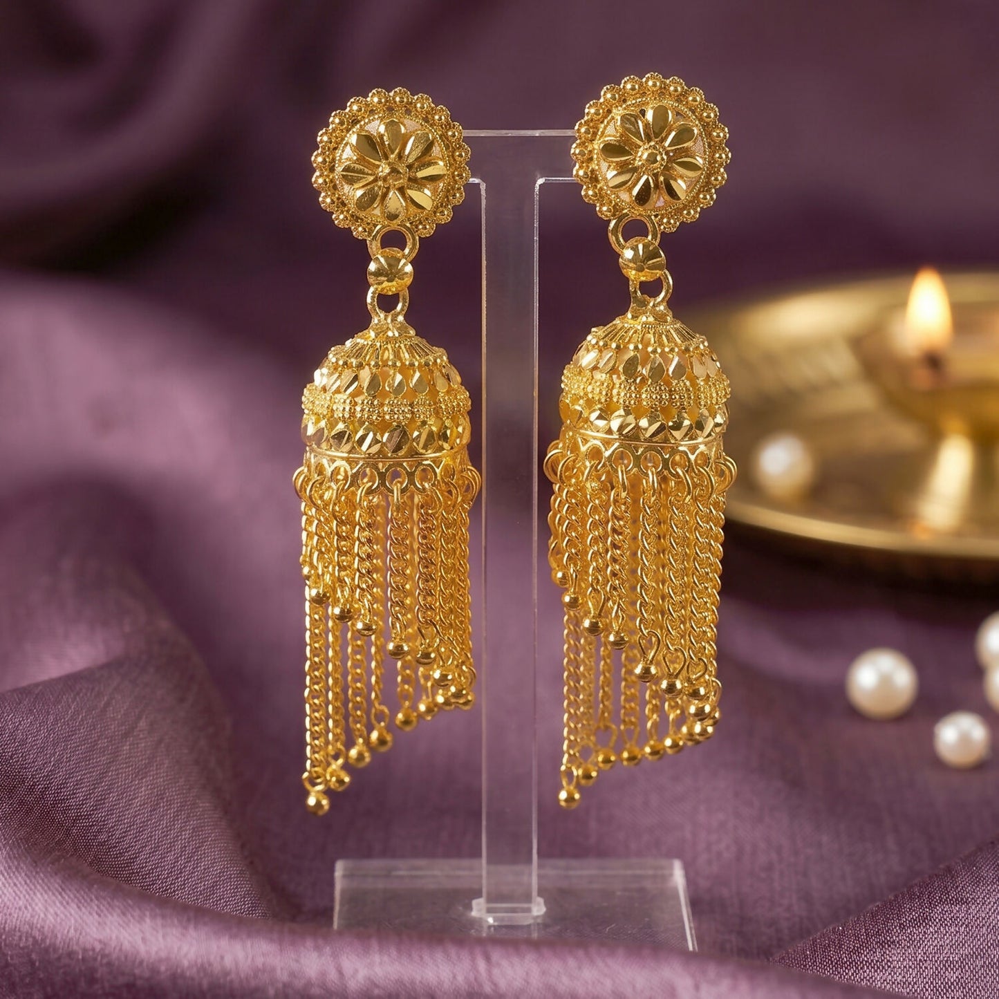 Golden jhumka earrings displayed on fabric background