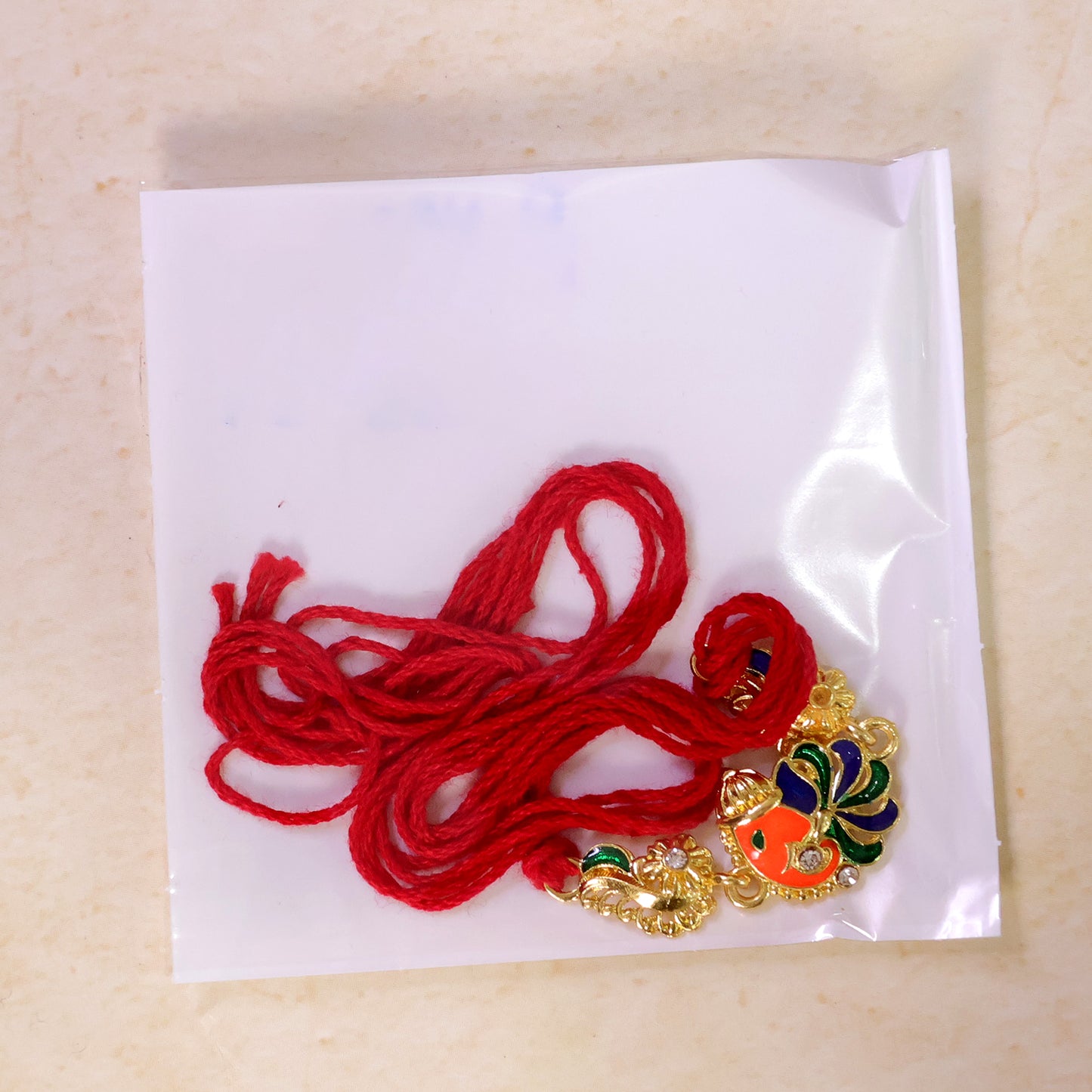 Gold-Toned Lord Ganesha Rakhi with Peacock Feather Enamel, Crystal Accents & Designer Red Thread