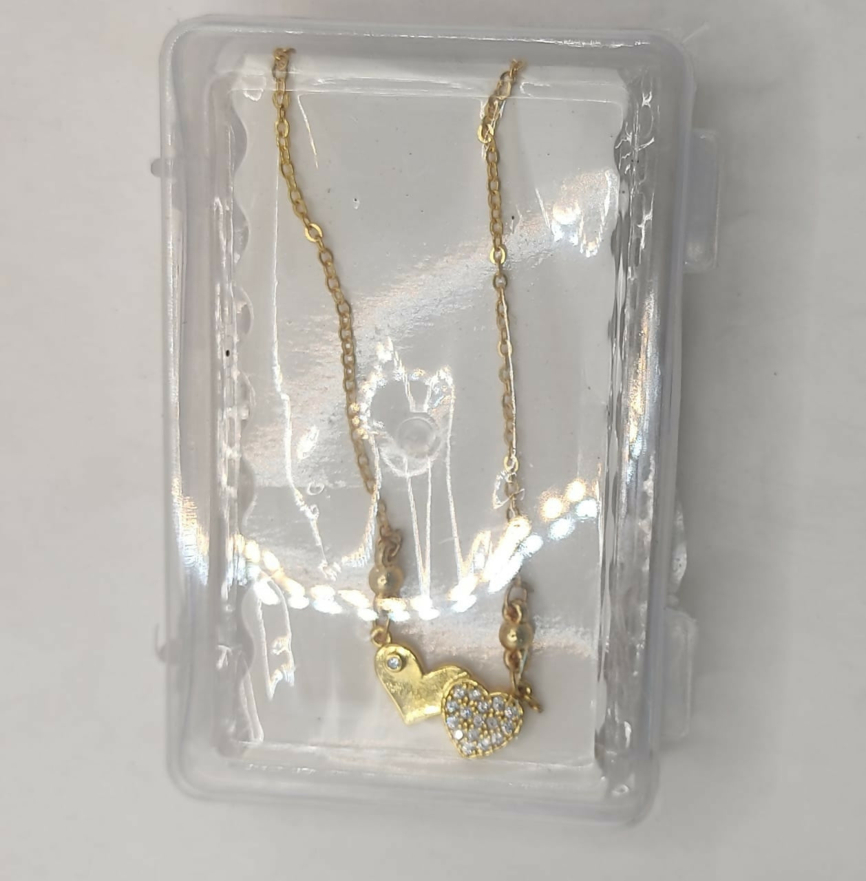 Two heart pendants on a gold plated chain necklace symbolizing connection and love