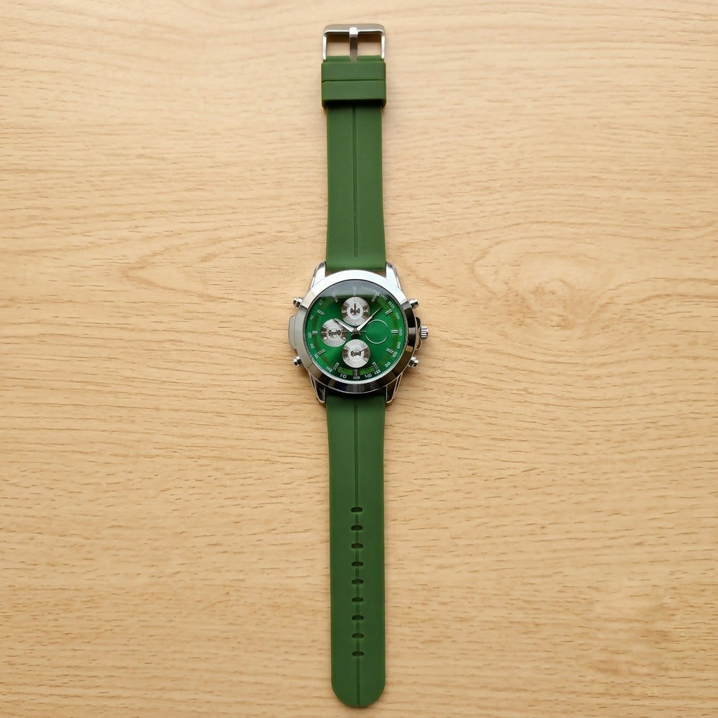 A green watch with a silver case and rubber strap, viewed from directly above on a light wooden background.