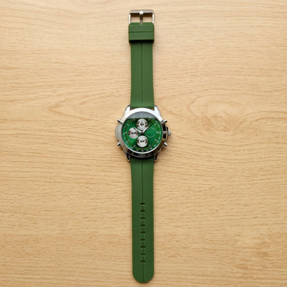 A green watch with a silver case and rubber strap, viewed from directly above on a light wooden background.